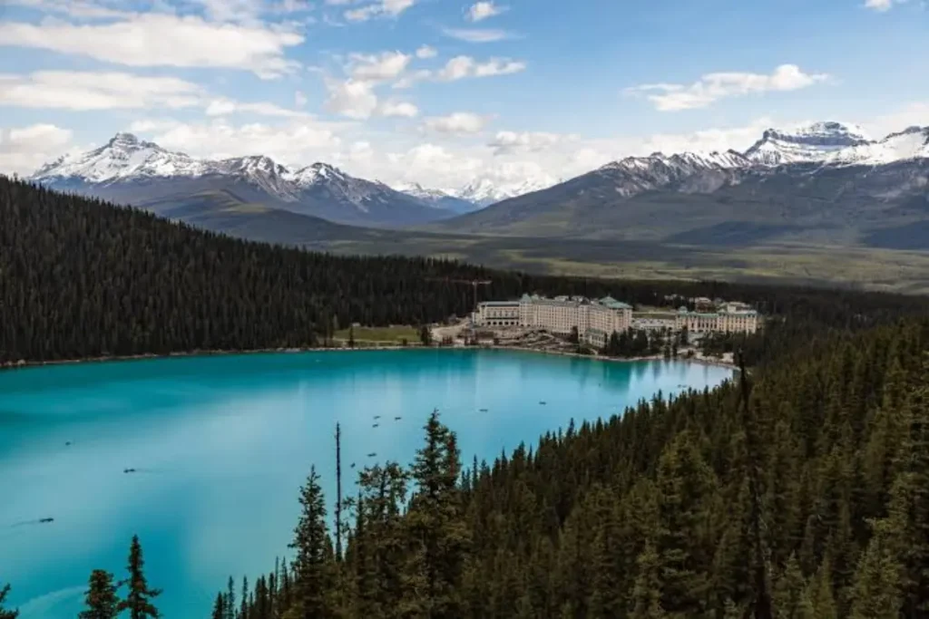 Panoramic view of turquoise Lake Louise and the Fairmont Chateau surrounded by pine forests and snow-capped mountains, ideal for family shore walks in Banff National Park