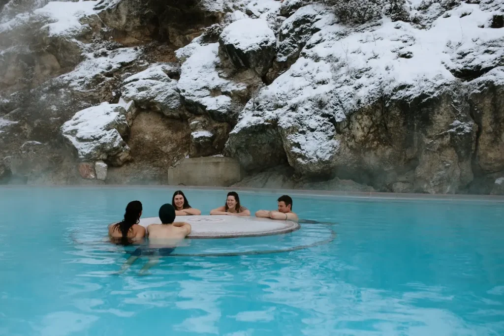 People relaxing in outdoor hot springs pool surrounded by snowy cliffs in soak at radium hot springs kootenay national park